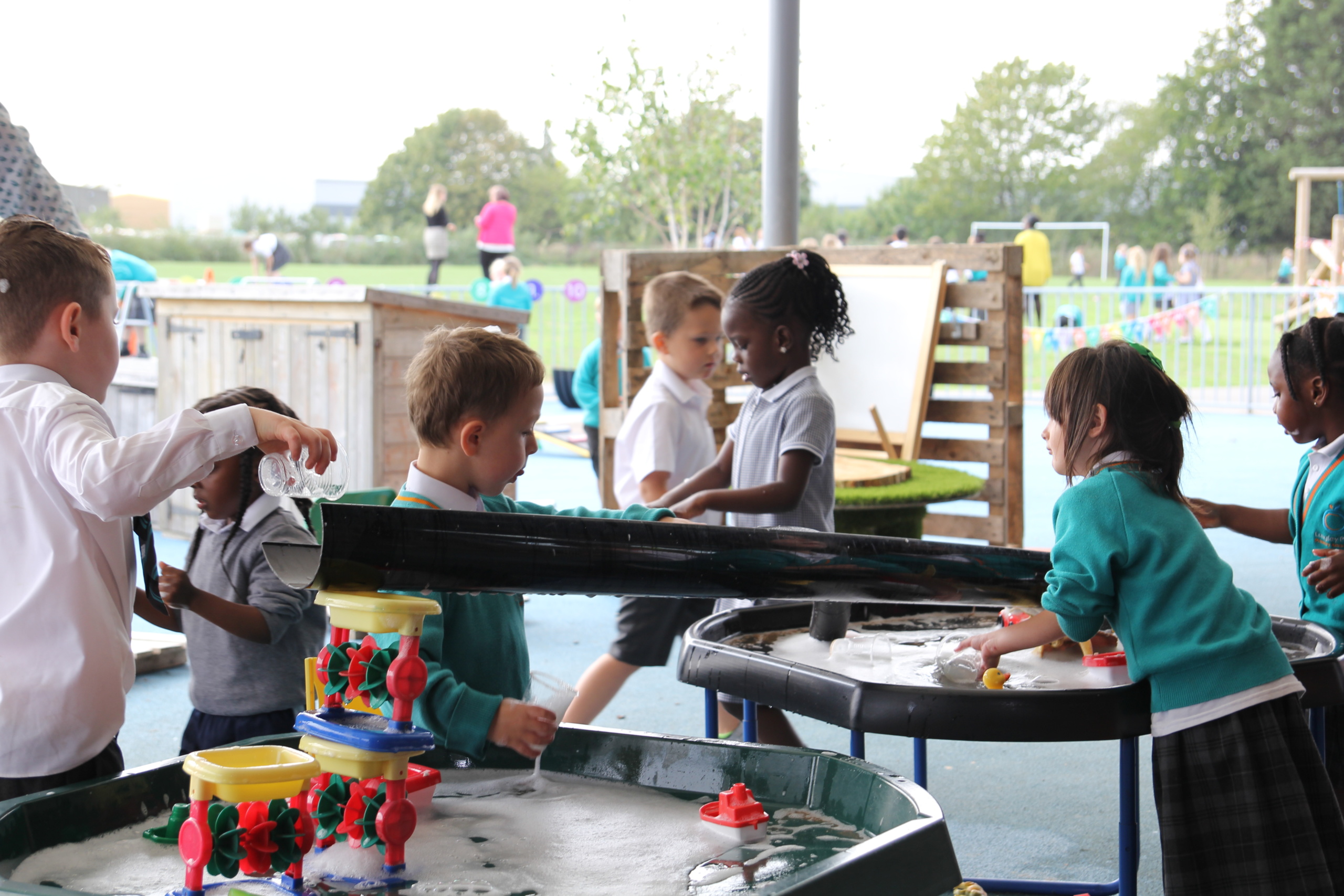 Many children playing in a water play set outdoors.