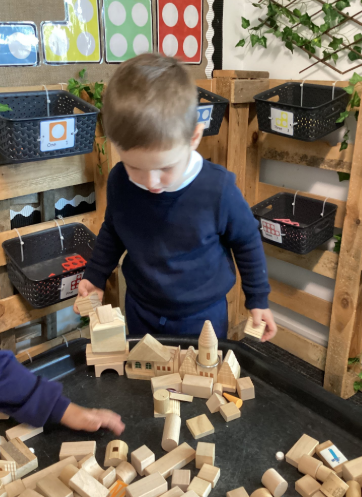 A young child in a uniform playing with a large collection of wooden building blocks, creating structures on a low table.