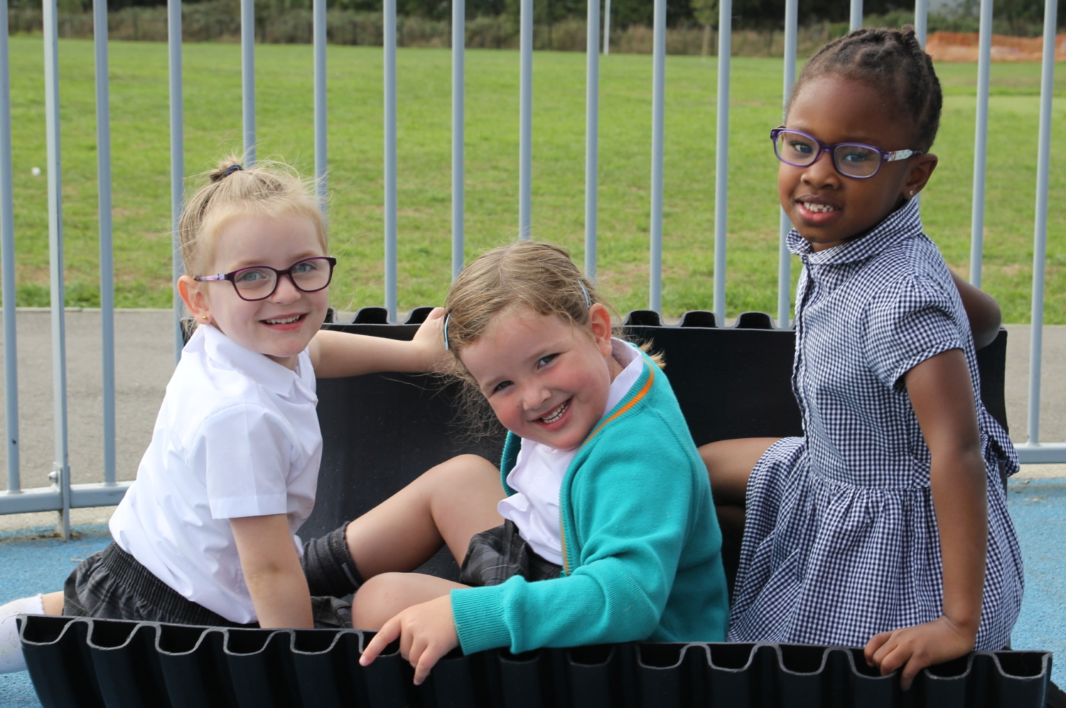 Three young children sitting in a tyre toy, turning backwards and smiling for the camera.