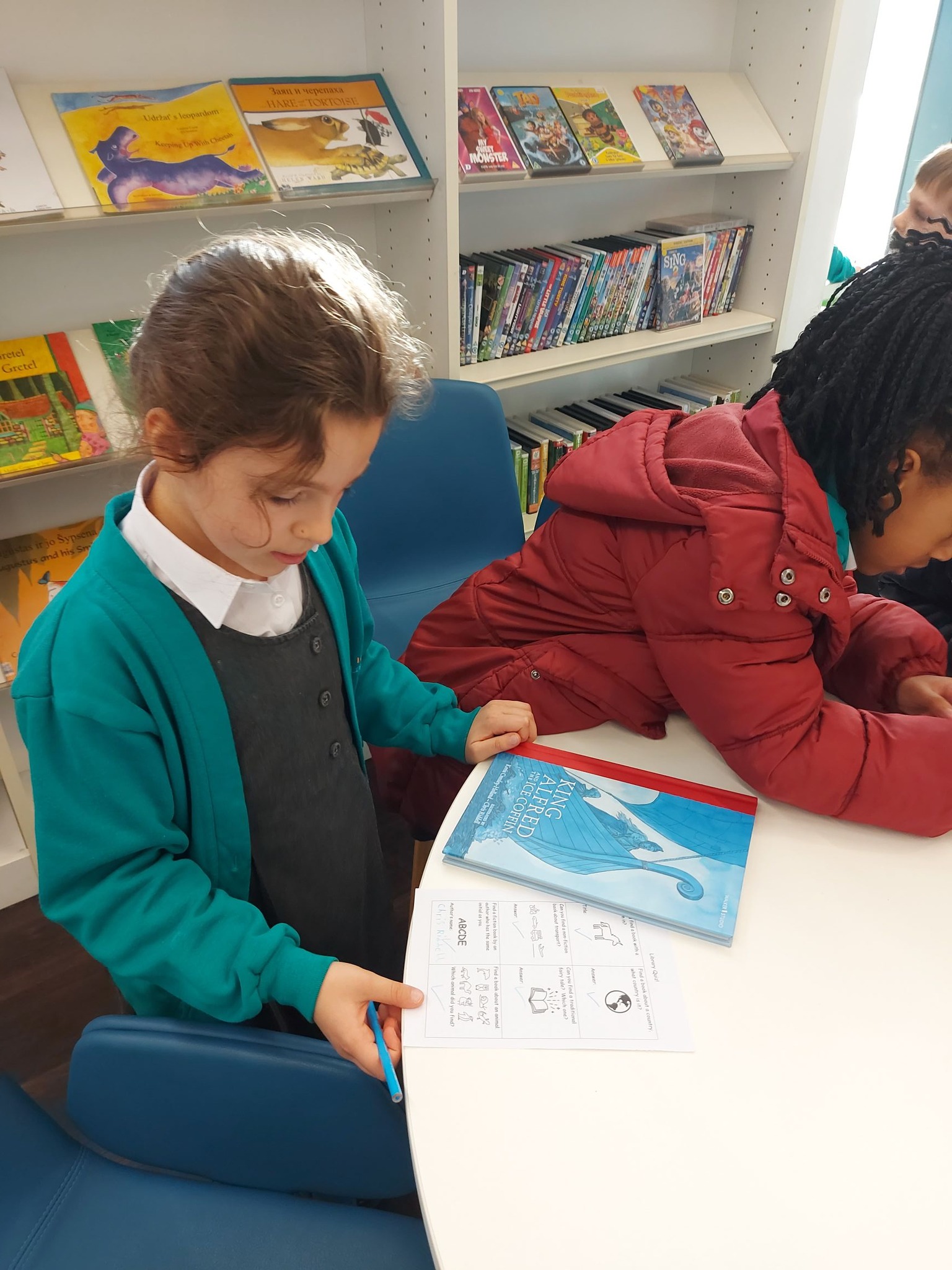 2 children at a table in a library looking at a book